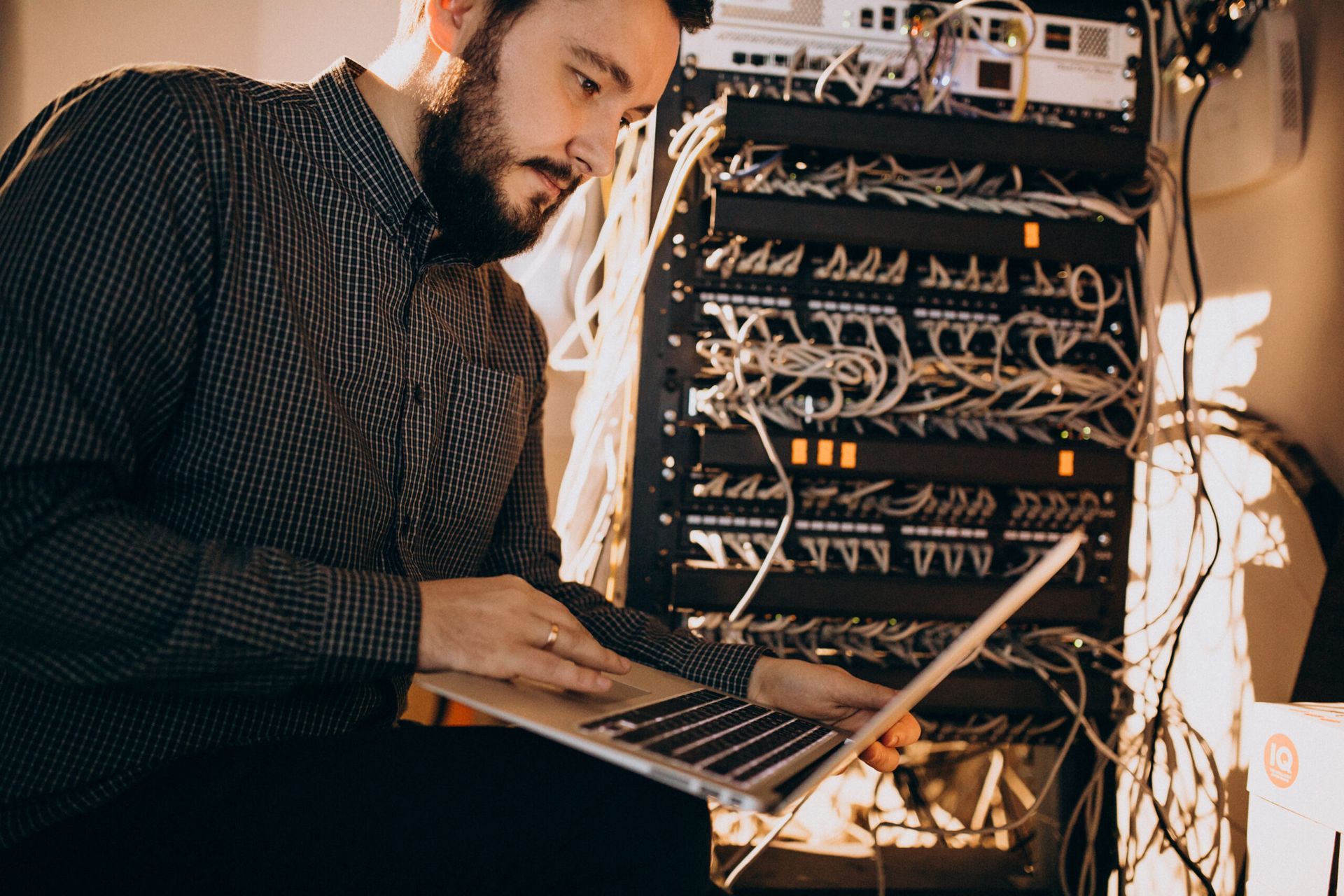 Un homme utilise un ordinateur portable devant un rack de serveur.