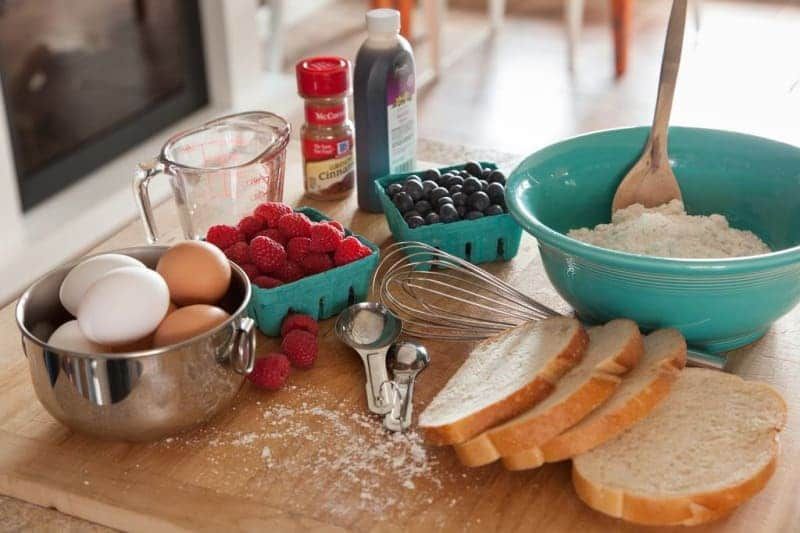 A cutting board with eggs , raspberries , blueberries and bread on it
