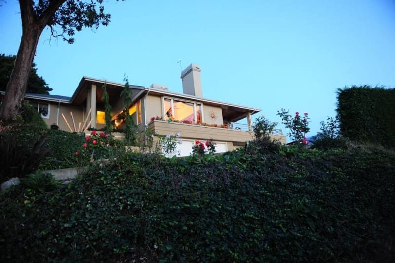 A large house sits on top of a hill surrounded by bushes and trees