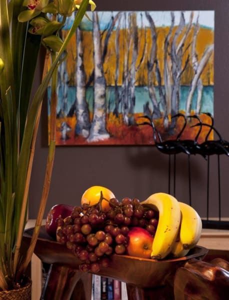 A bowl of fruit sits in front of a painting of trees