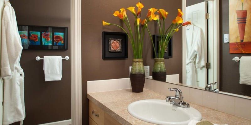 A bathroom with a sink , mirror and vases of flowers.