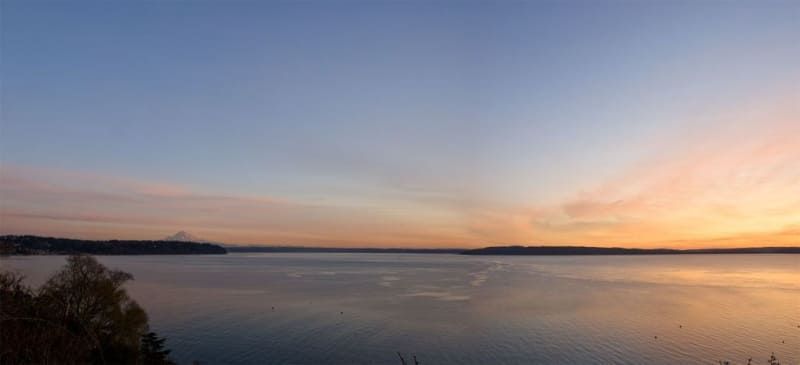 A sunset over a large body of water with trees in the foreground.