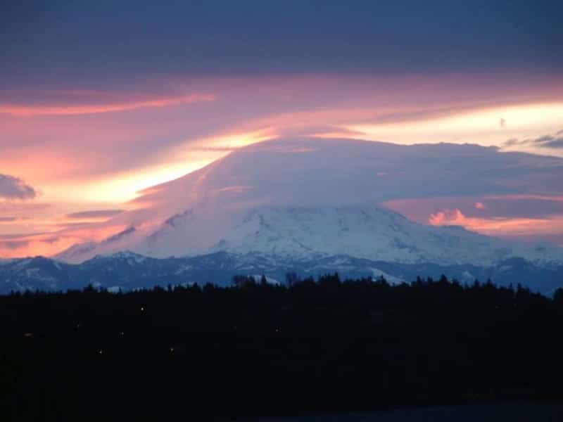 A mountain covered in snow is silhouetted against a sunset sky