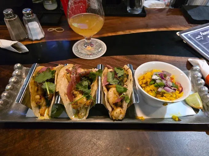 Tray of tacos and a bowl of soup on a bar counter with a margarita glass in the background