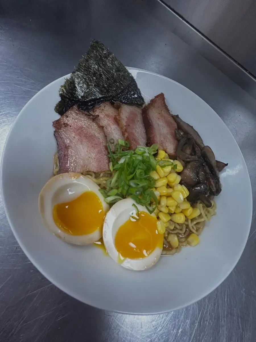 Ramen bowl with sliced pork, soft-boiled eggs, corn, green onions, mushrooms, and nori on a white plate