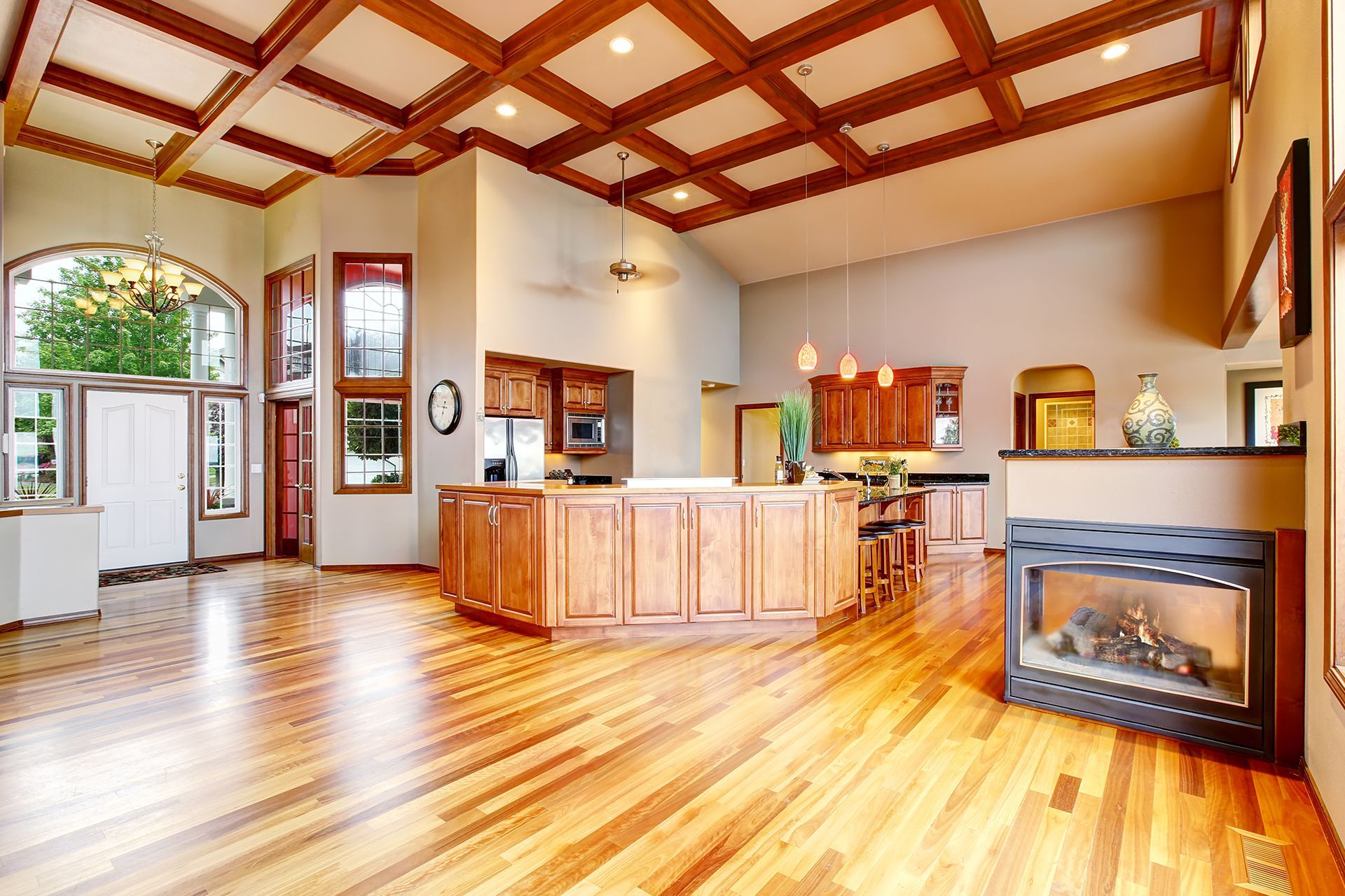 Spacious, well-lit living room with hardwood floors, a coffered ceiling, a kitchen island, and a fireplace. Spacious, well-lit living room with hardwood floors, a coffered ceiling, a kitchen island, and a fireplace.