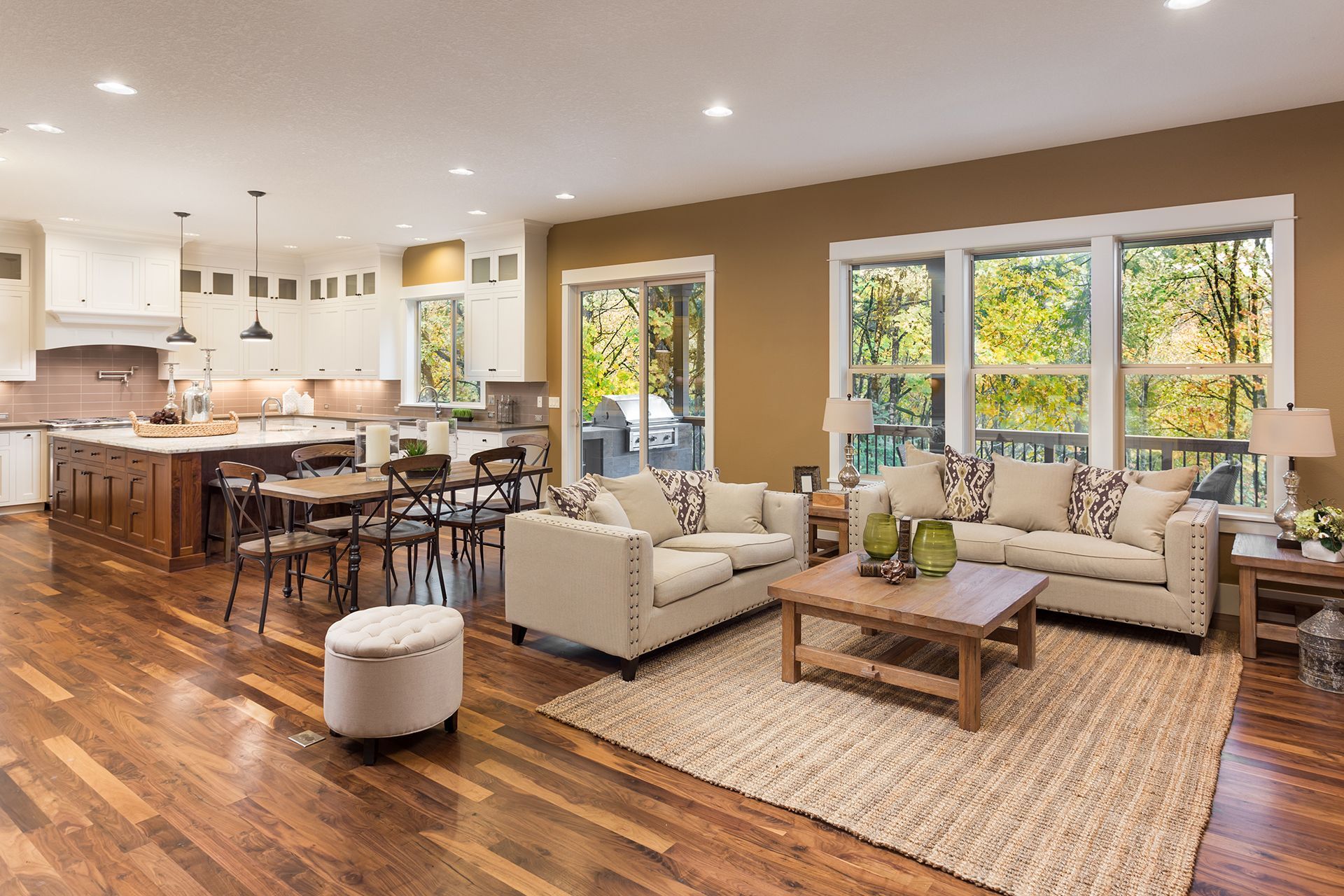 Spacious open-concept living space with kitchen and living room; hardwood floors, neutral-colored furniture, and large windows.