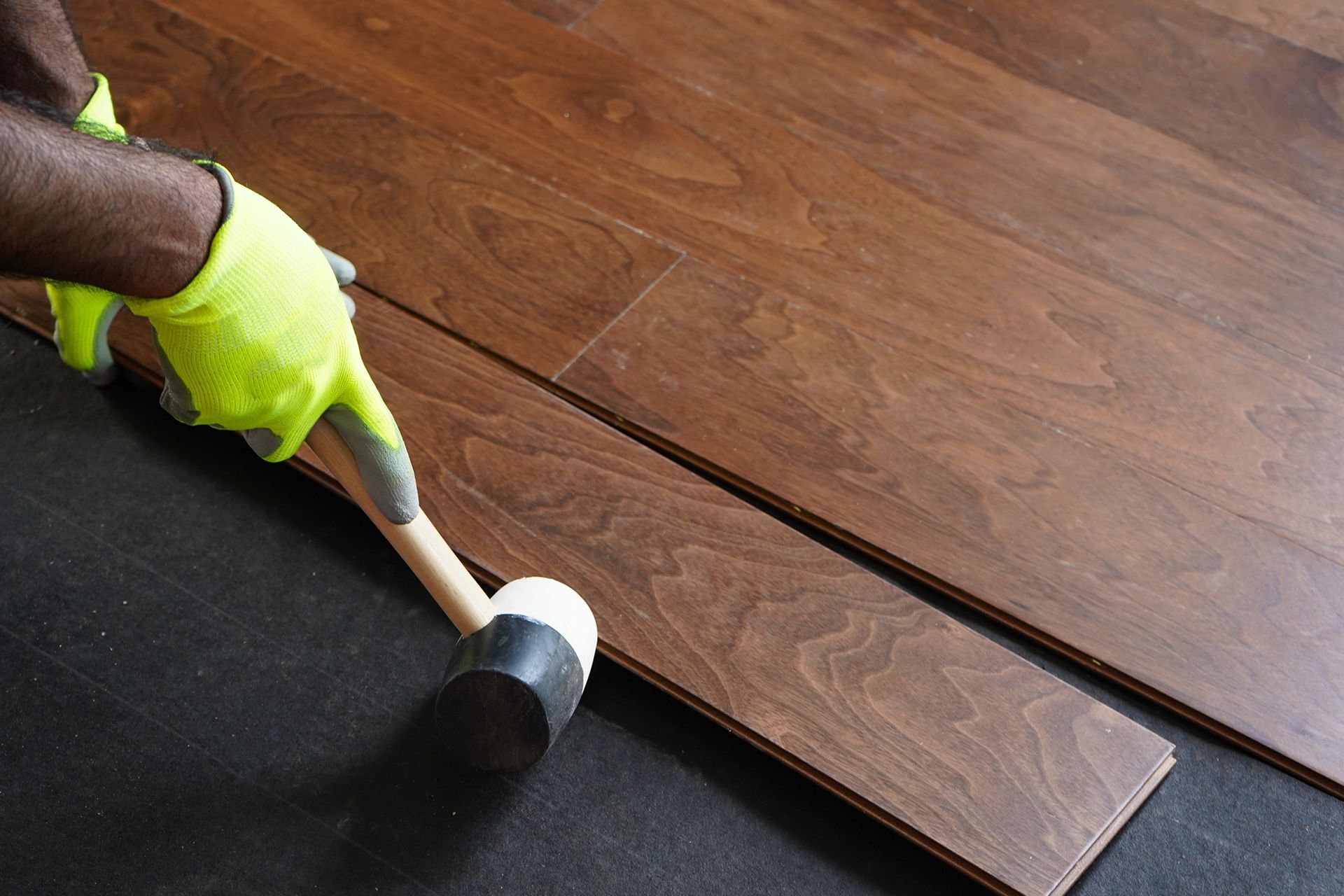 Person installing dark wood flooring, using a hammer and gloves. Person installing dark wood flooring, using a hammer and gloves.