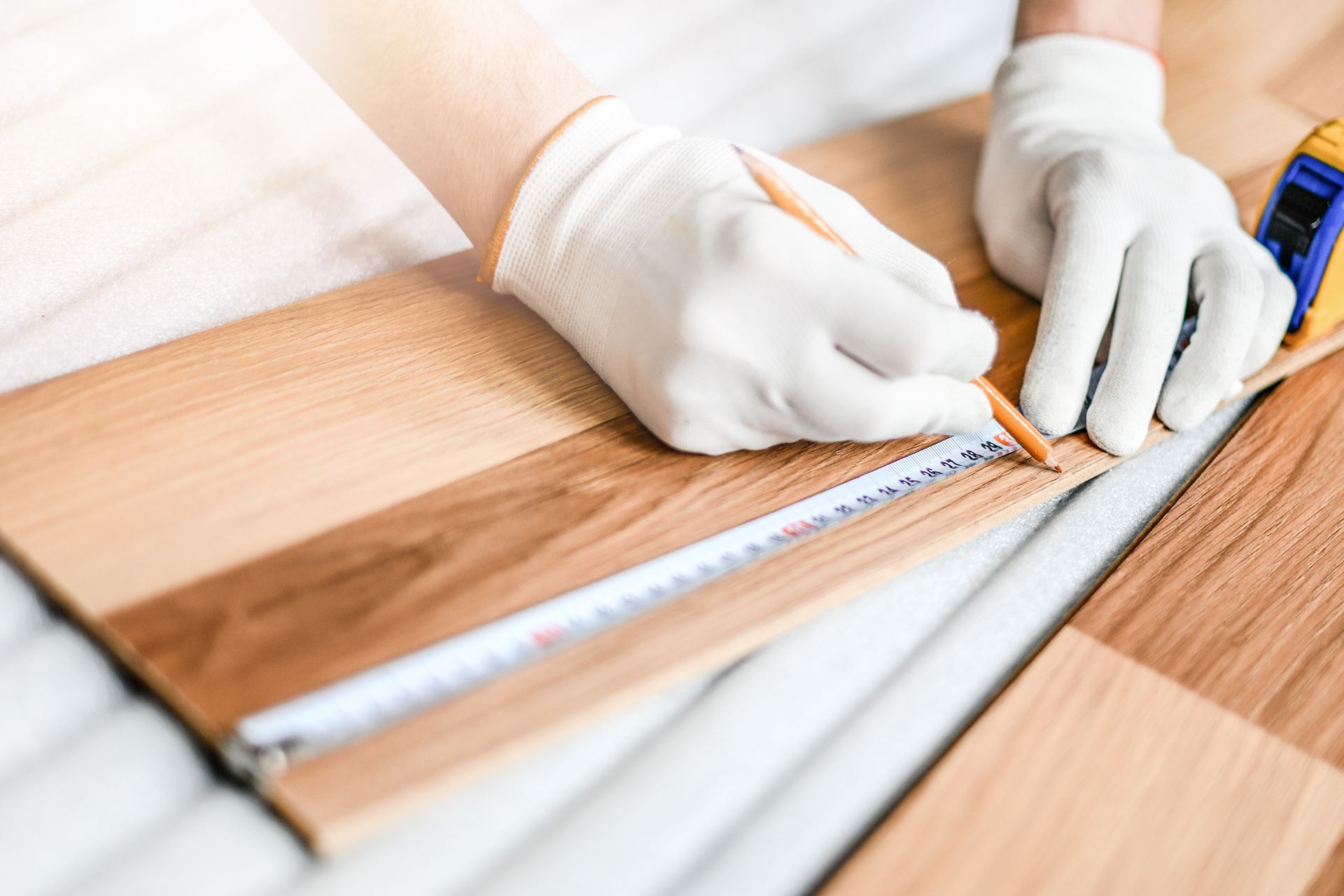 Person wearing gloves marks wood flooring with pencil and measuring tape. Person wearing gloves marks wood flooring with pencil and measuring tape.