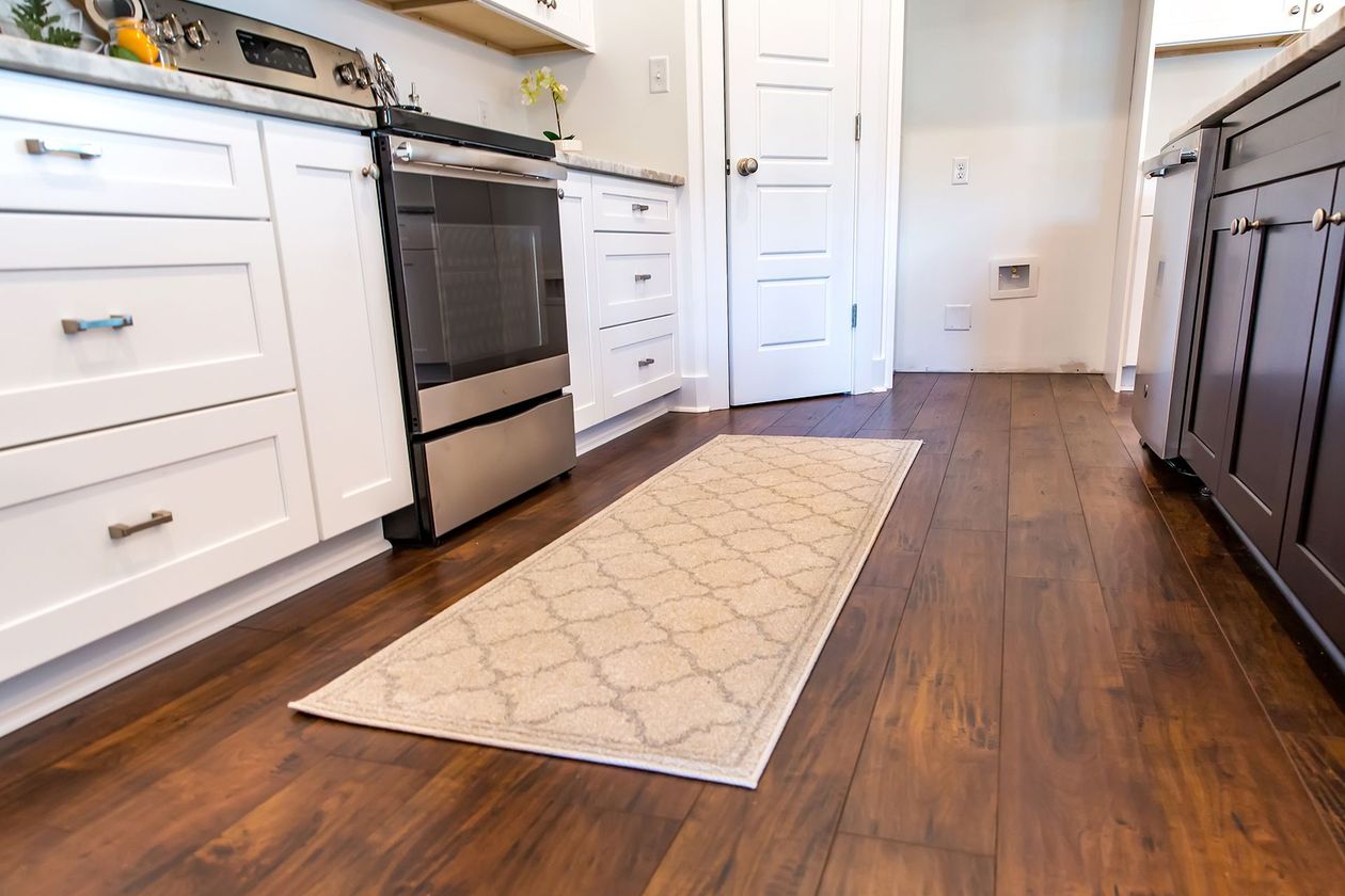 Kitchen with white cabinets, stainless steel oven, wood floors, and a patterned rug. Kitchen with white cabinets, stainless steel oven, wood floors, and a patterned rug.