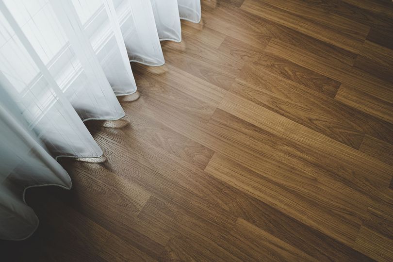 White sheer curtain draped over light brown hardwood floor. White sheer curtain draped over light brown hardwood floor.