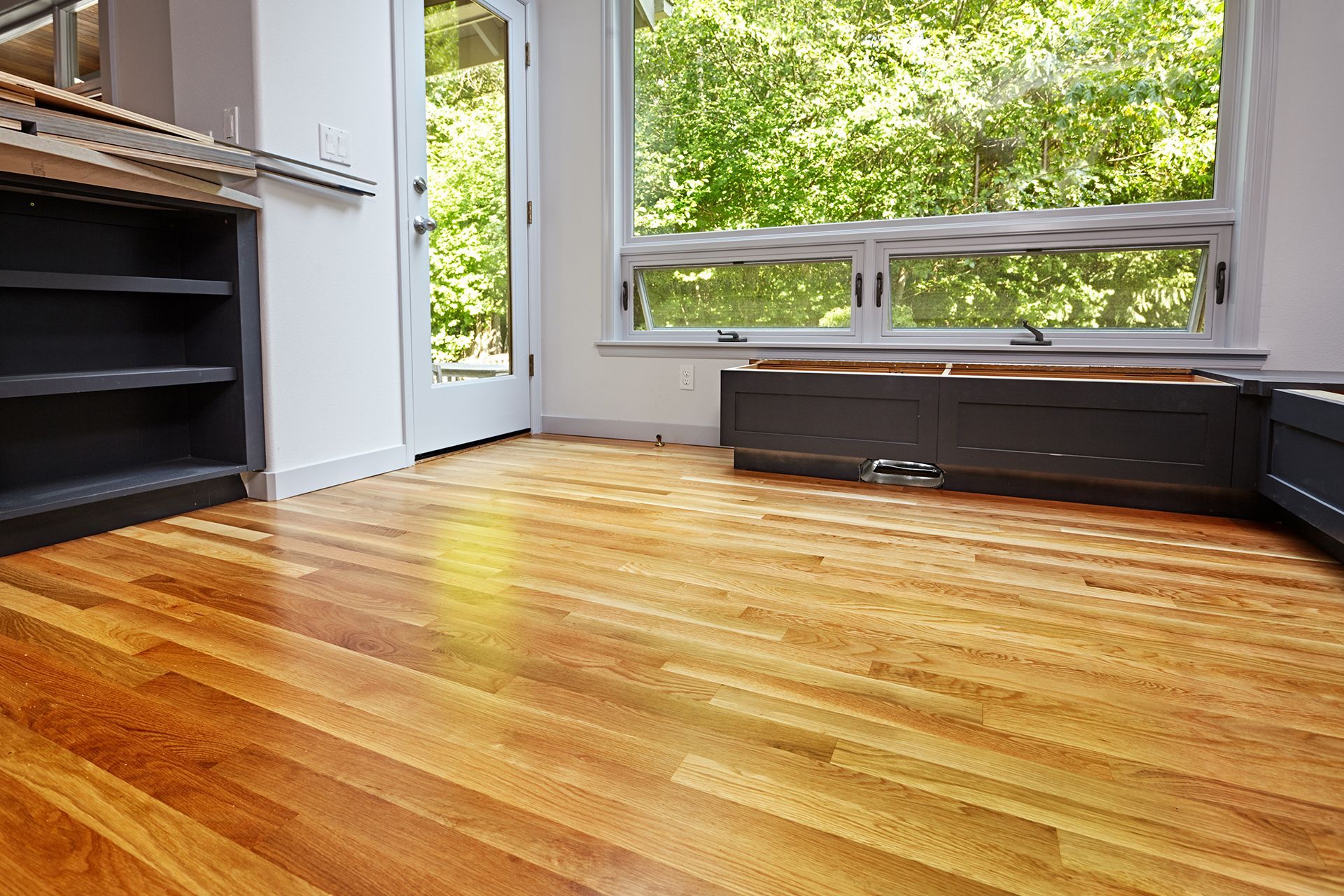 Hardwood floor in a room with a window overlooking trees; a dark cabinet is in the background. Hardwood floor in a room with a window overlooking trees; a dark cabinet is in the background.