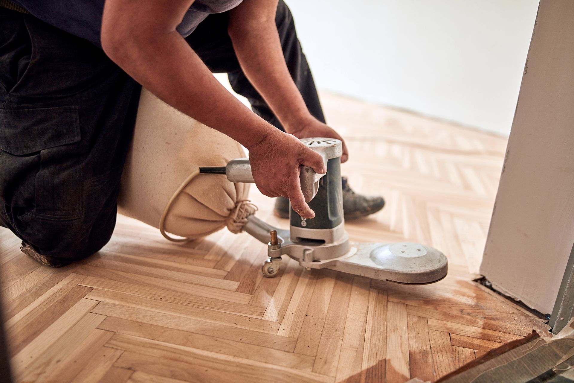 Person sanding parquet flooring with a disc sander, dust bag attached. Person sanding parquet flooring with a disc sander, dust bag attached.