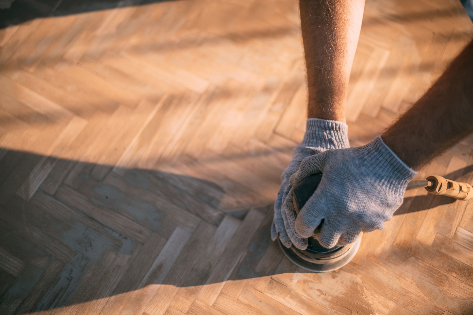 Person sanding wooden floor with a handheld sander. Person sanding wooden floor with a handheld sander.