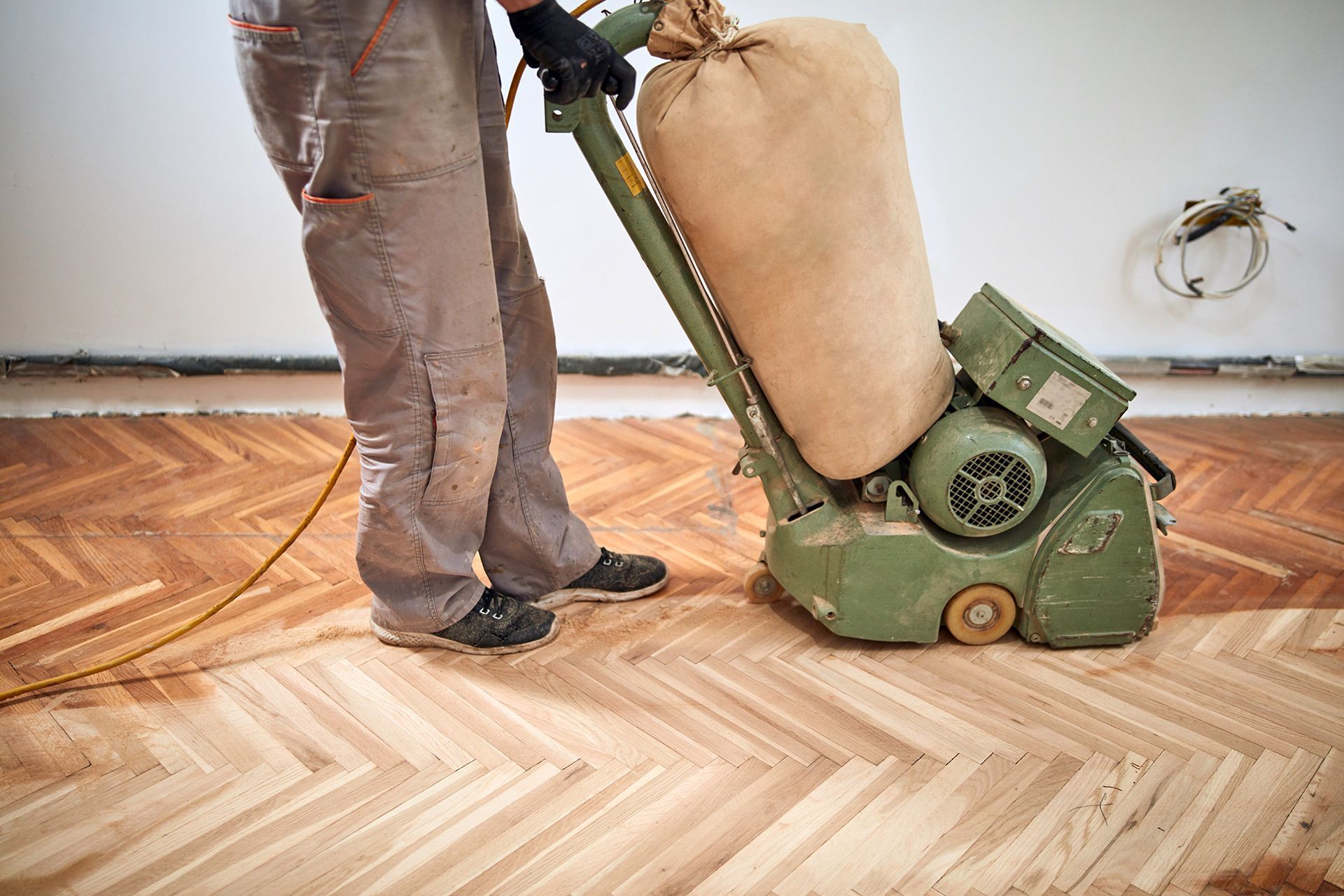 Person sanding a wooden herringbone floor with a large industrial sander, indoors. Person sanding a wooden herringbone floor with a large industrial sander, indoors.