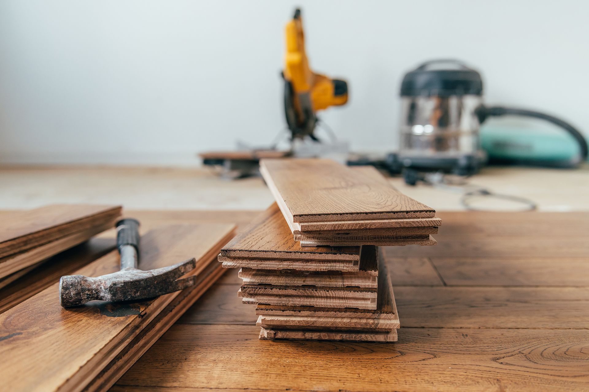 Wooden floorboards stacked with tools: hammer, saw, and vacuum, likely for installation. Wooden floorboards stacked with tools: hammer, saw, and vacuum, likely for installation.