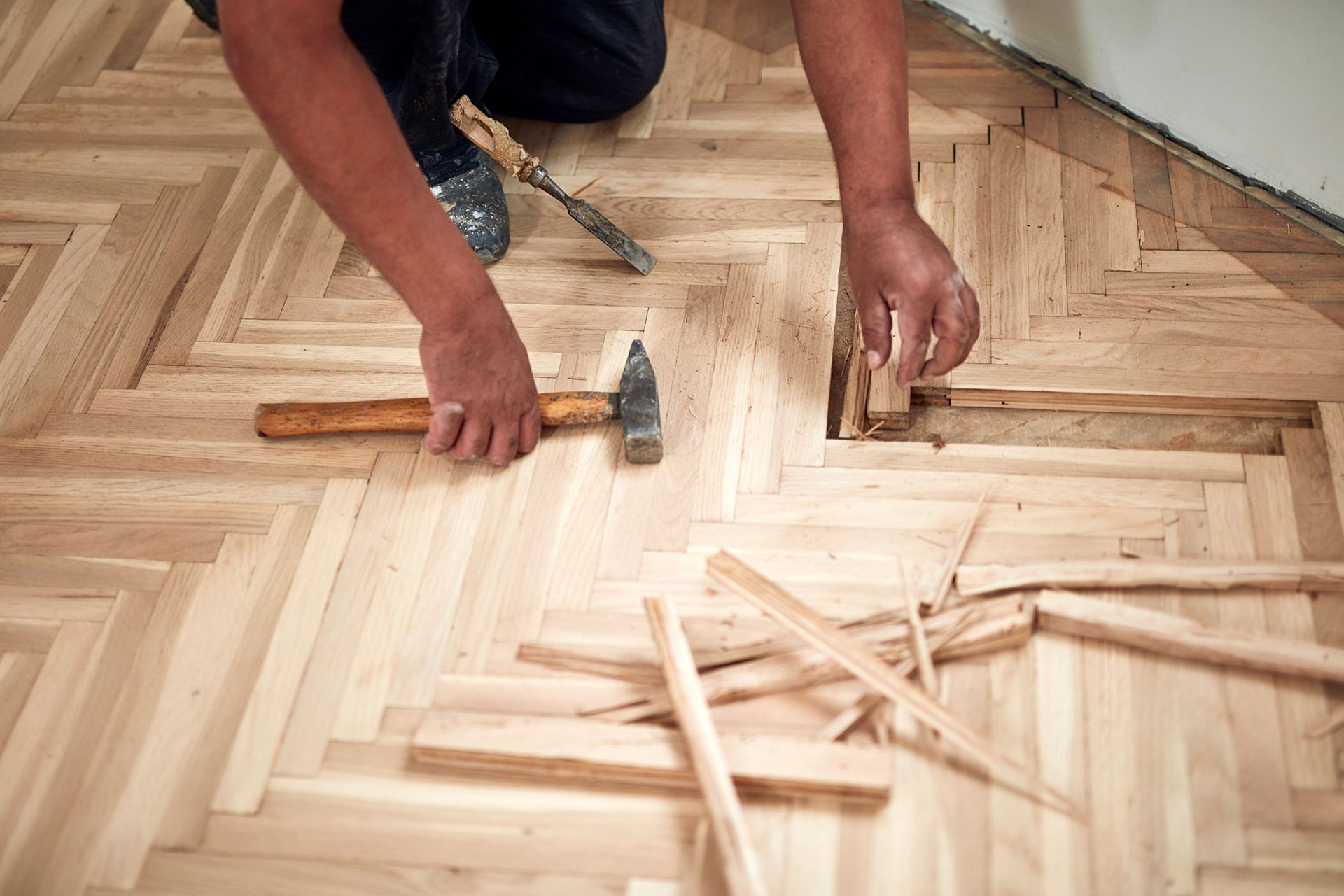 Person installing hardwood parquet flooring, using hammer and chisel. Person installing hardwood parquet flooring, using hammer and chisel.