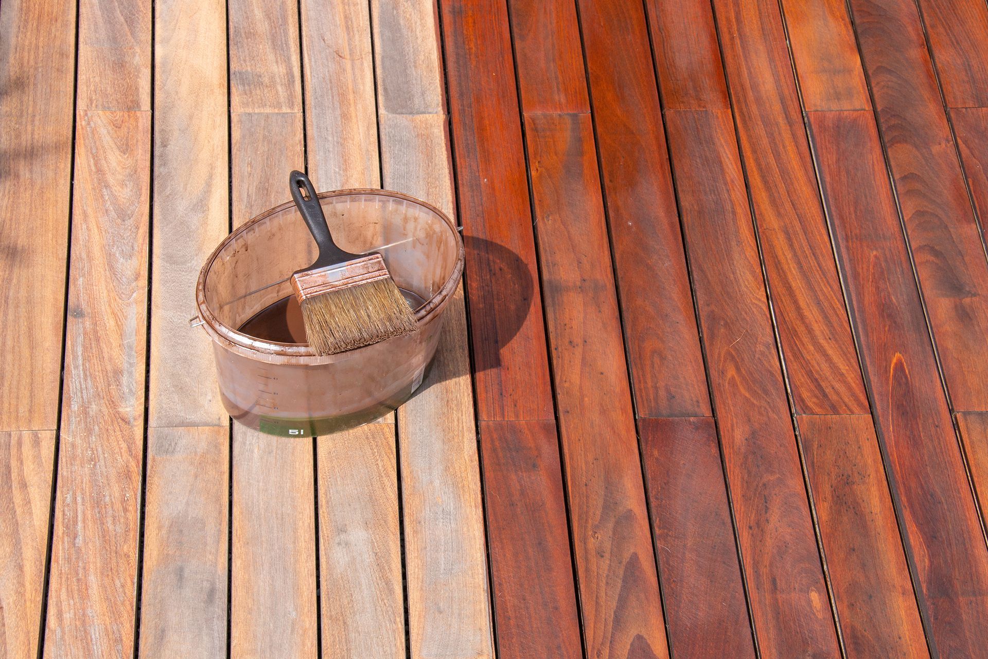 Wooden deck, half stained dark brown, with a bucket and brush. Wooden deck, half stained dark brown, with a bucket and brush.