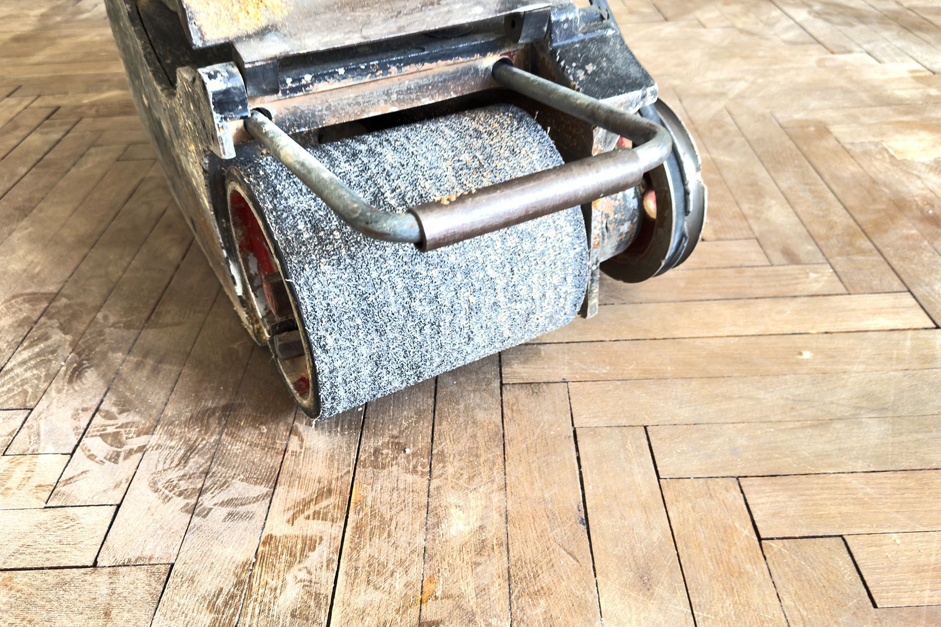 Floor sander on a wooden floor, close-up. The machine has a large abrasive roller, and a metal handle. Floor sander on a wooden floor, close-up. The machine has a large abrasive roller, and a metal handle.