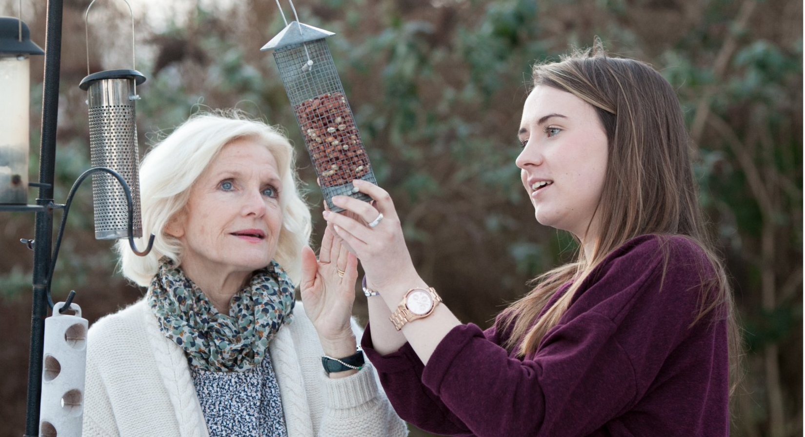 Elderly lady with carer checking a bird feeder