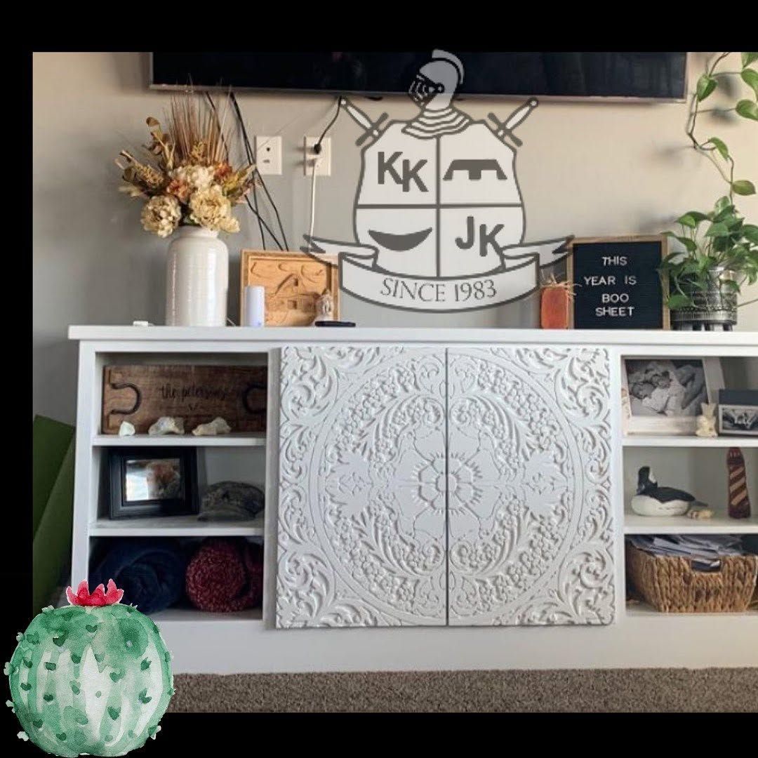 White cabinet with decorative wall sign, shelves, baskets, flowers, and a cactus on the floor.