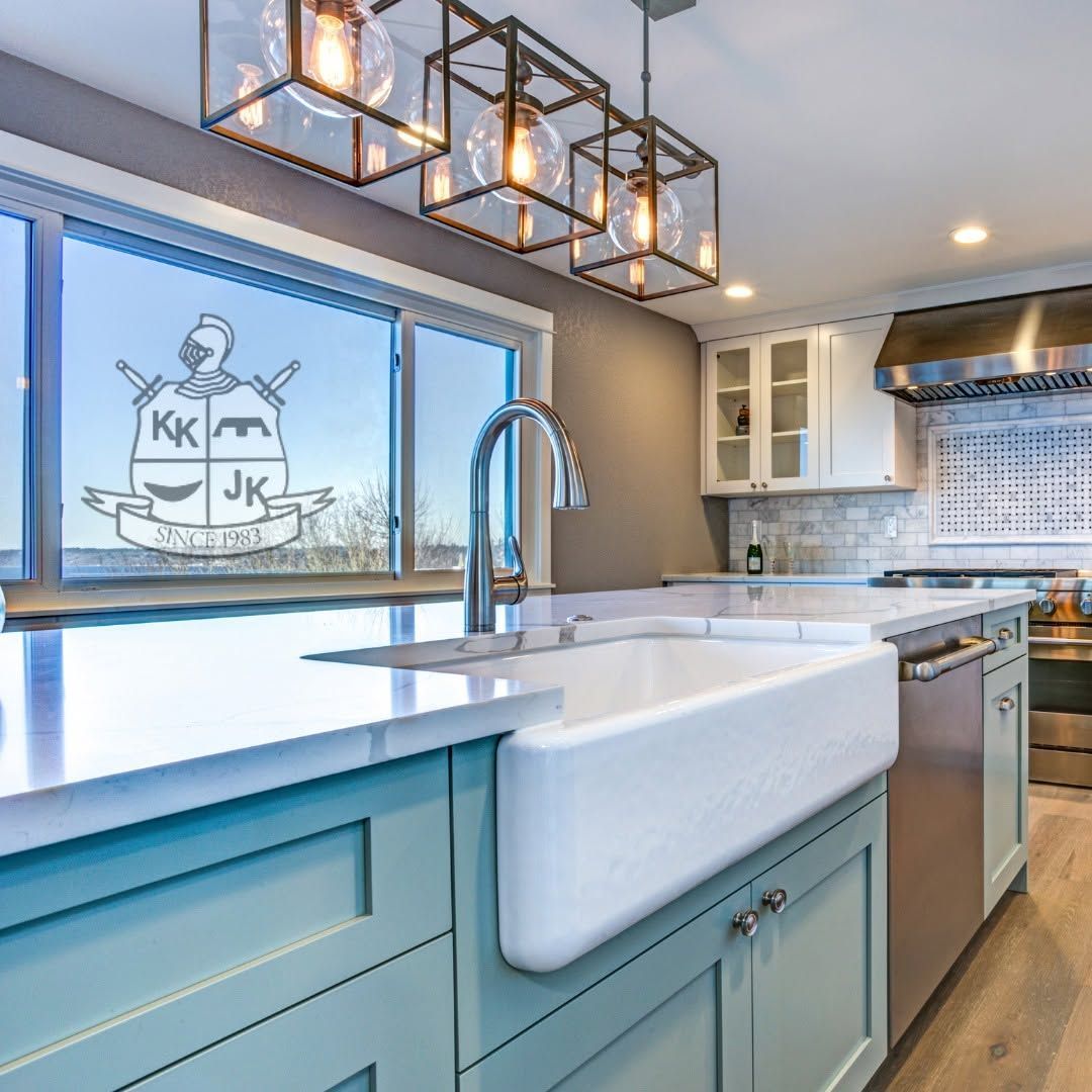 Bright modern kitchen with white farmhouse sink, blue cabinets, pendant lights, and a window above the sink