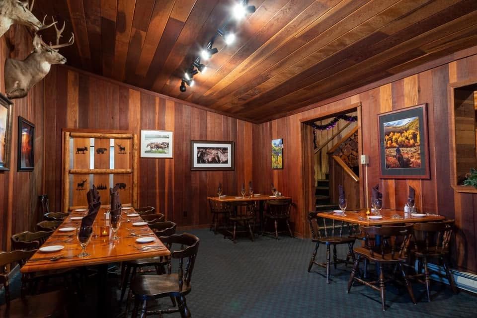Wood-paneled restaurant dining room with long wooden tables, framed art, and moose heads on the walls