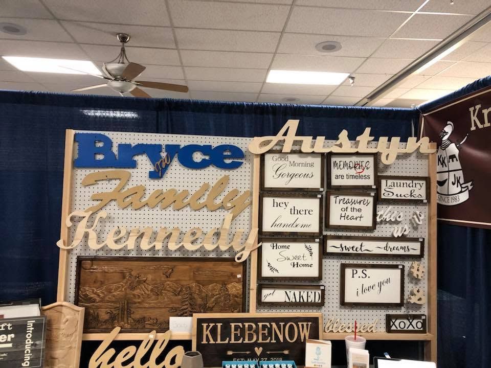 Assorted wooden name signs displayed on a blue curtain backdrop at a craft booth