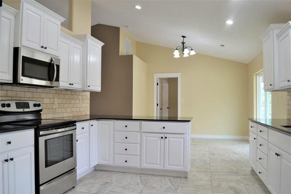 Bright modern kitchen with white cabinets, black appliances, and light tile flooring