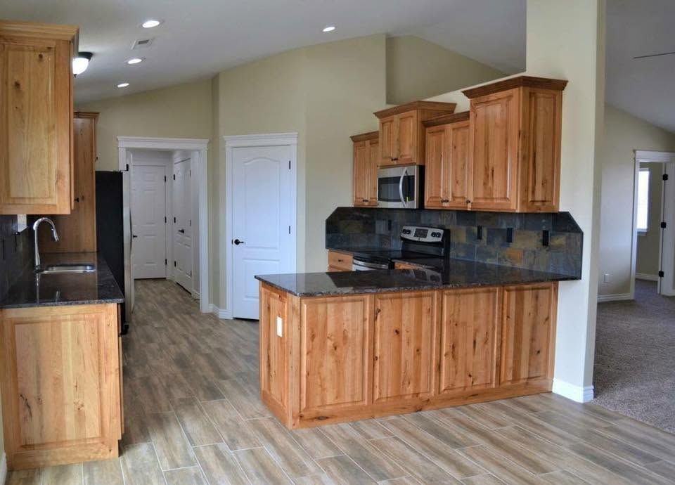 Empty modern kitchen with wood cabinets, dark countertops, and light wood flooring in an open floor plan