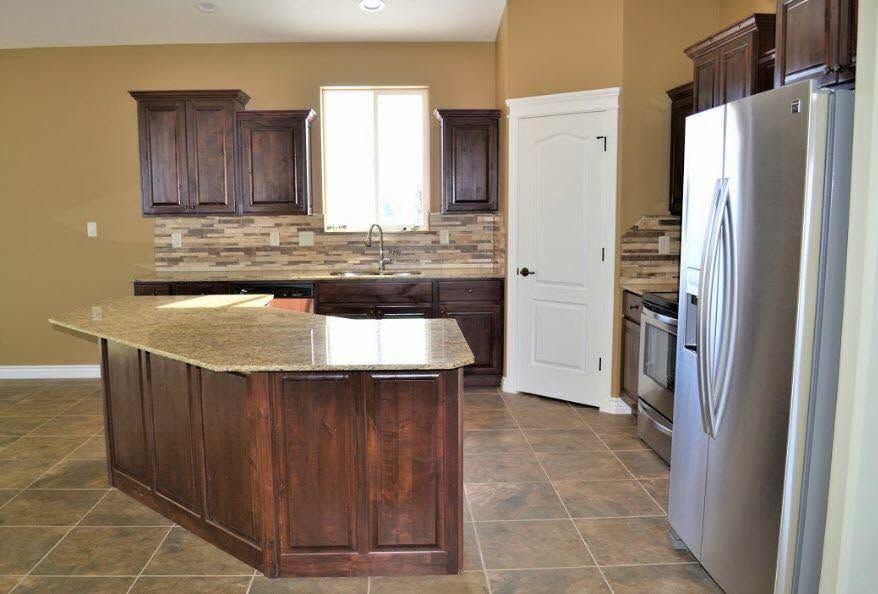 Modern kitchen with dark wood cabinets, granite island, tile floor, and stainless steel refrigerator