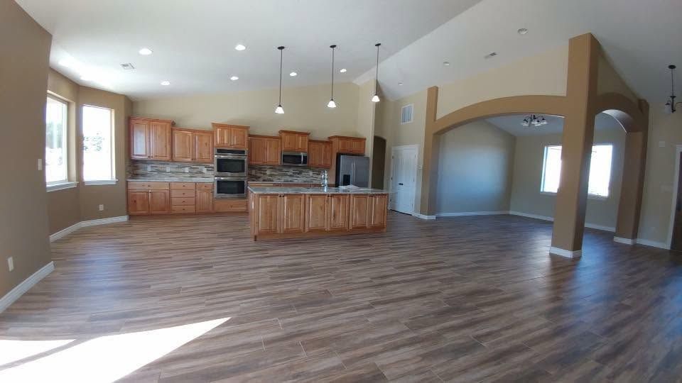 Open-plan kitchen and living room with wood floors, tan walls, island, and large windows