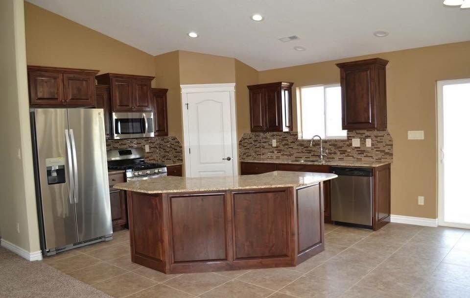 Empty modern kitchen with dark wood cabinets, stainless steel appliances, and a large island