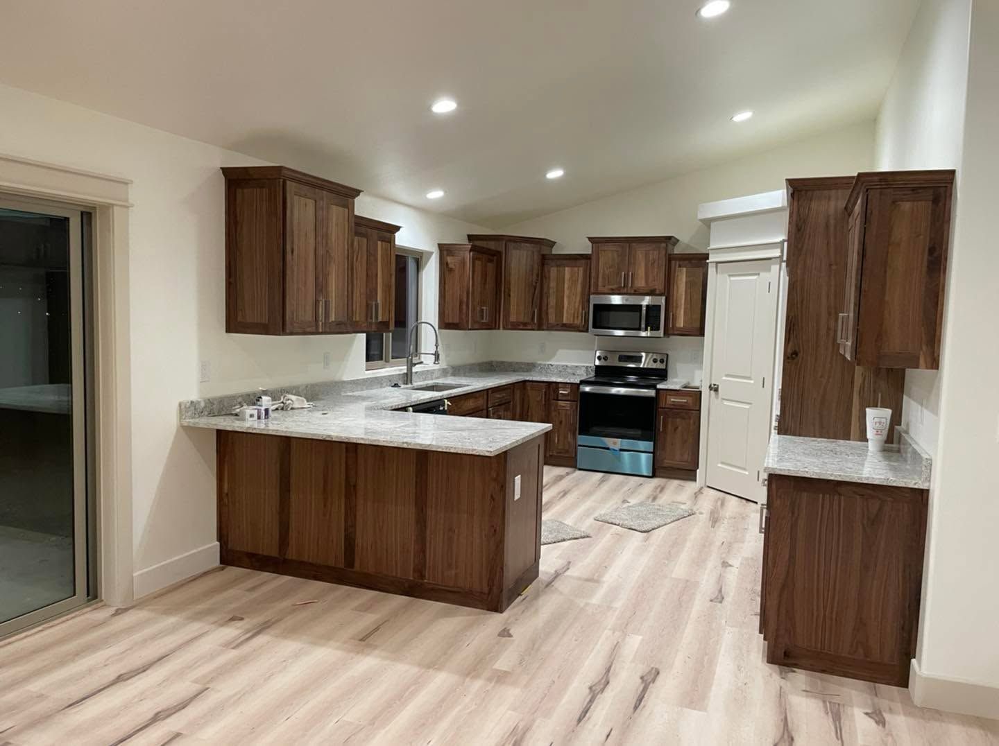 Empty modern kitchen with wood cabinets, granite counters, stainless appliances, and light wood floors