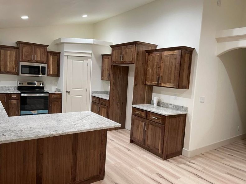 Modern kitchen with wood cabinets, granite island, stainless appliances, and light tile flooring.