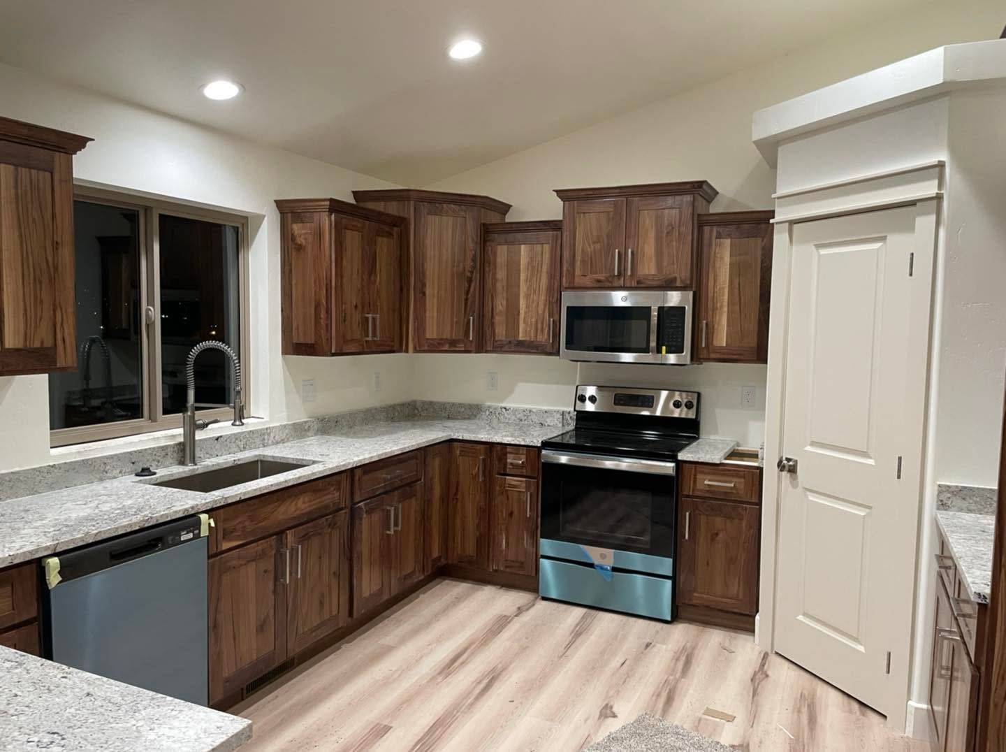 Modern kitchen with dark wood cabinets, granite counters, stainless appliances, and light wood floors.