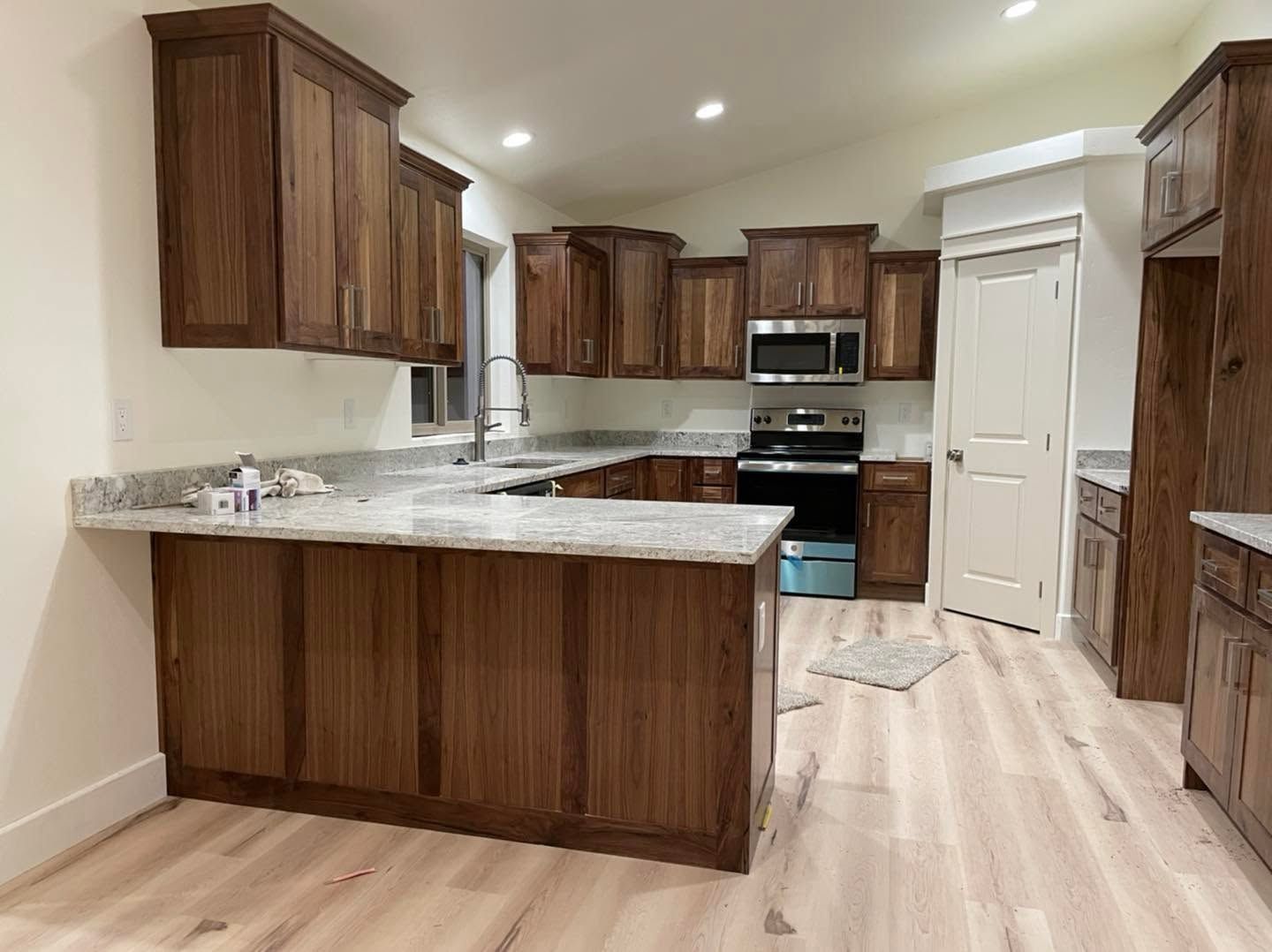 Modern kitchen with dark wood cabinets, white countertops, stainless appliances, and light wood floors.