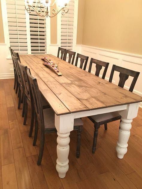 Long rustic dining table with white legs and dark chairs in a bright dining room