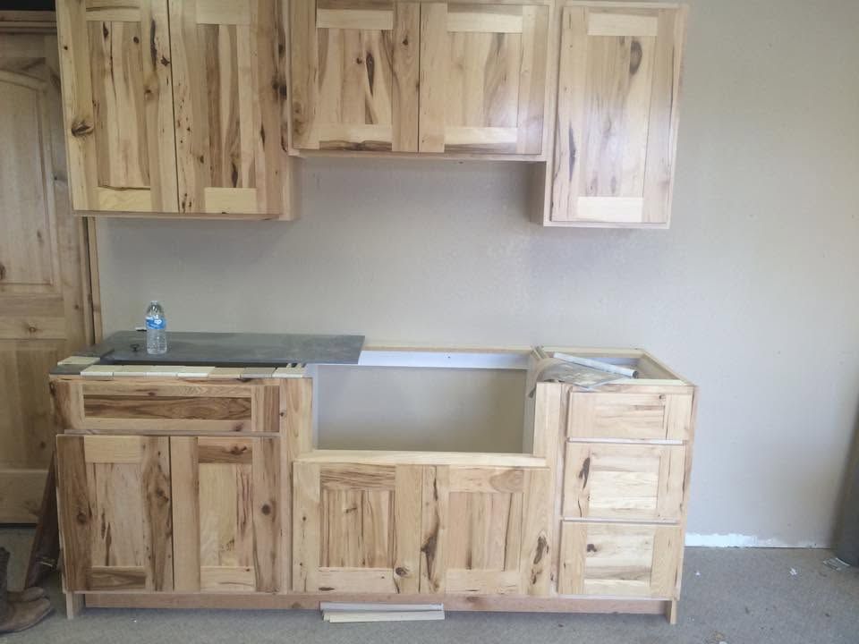 Unfinished wooden kitchen cabinets and sink base installed against a beige wall.
