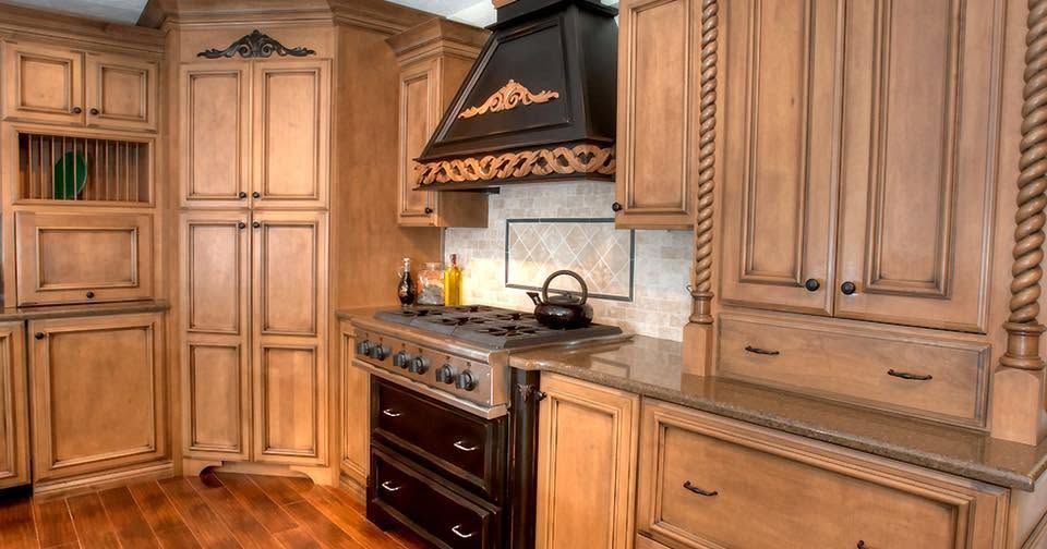 Wooden kitchen with gas stove, black range hood, and light wood cabinets, seen from a corner view