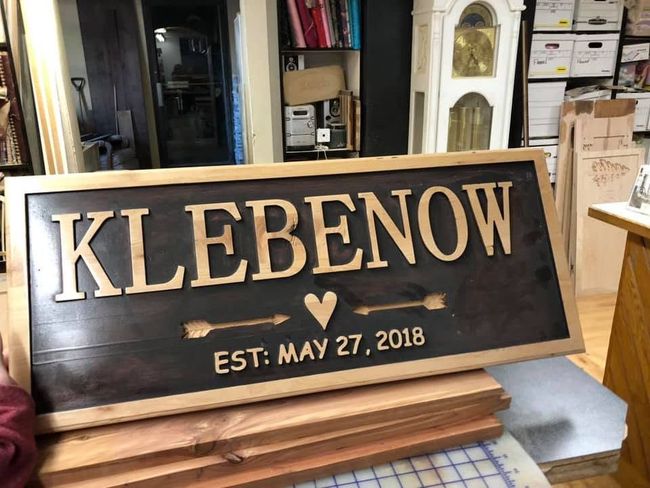 “KLEBENON” wooden sign with gold lettering, small heart, and “EST. MAY 27, 2018” on a workbench