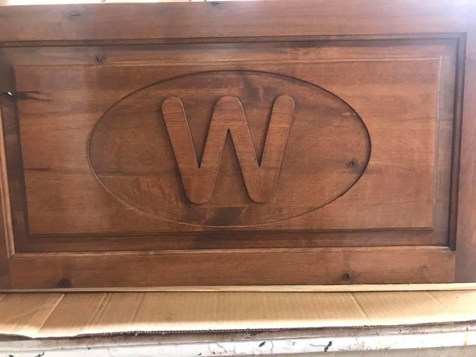 Wooden panel with a carved oval and large letter W on a tan wall.