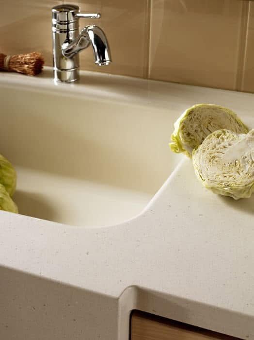 Kitchen sink with faucet and a head of lettuce on the white countertop