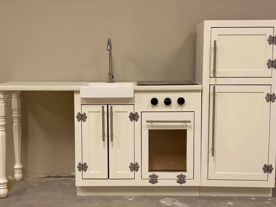 White toy kitchen set with sink, stove, and cabinets against a beige wall