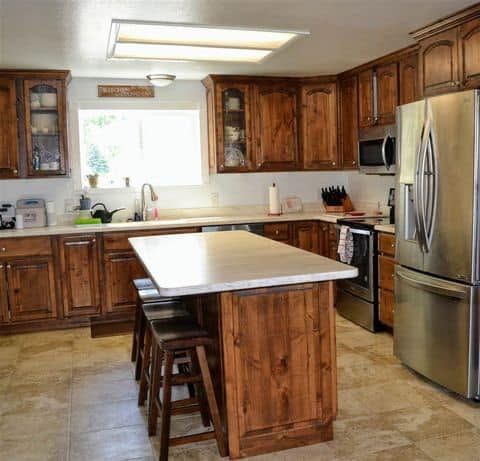 Cozy wood-paneled kitchen with stainless steel refrigerator, center island, and stools