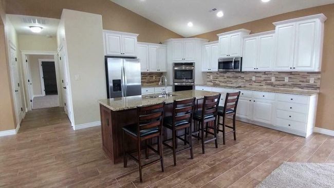 Bright modern kitchen with white cabinets, stainless appliances, wood floors, and a large island with barstools