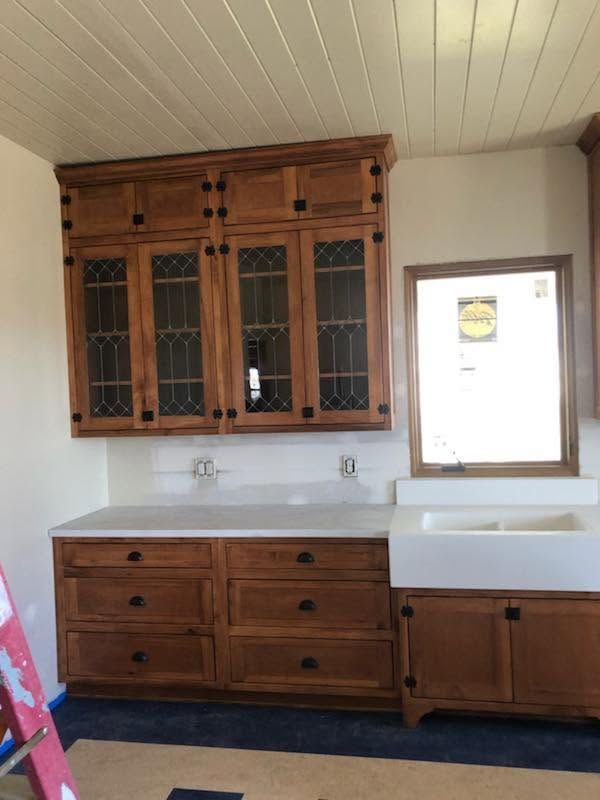 Wooden kitchen cabinets with white countertop and sink beneath a window, in a small room