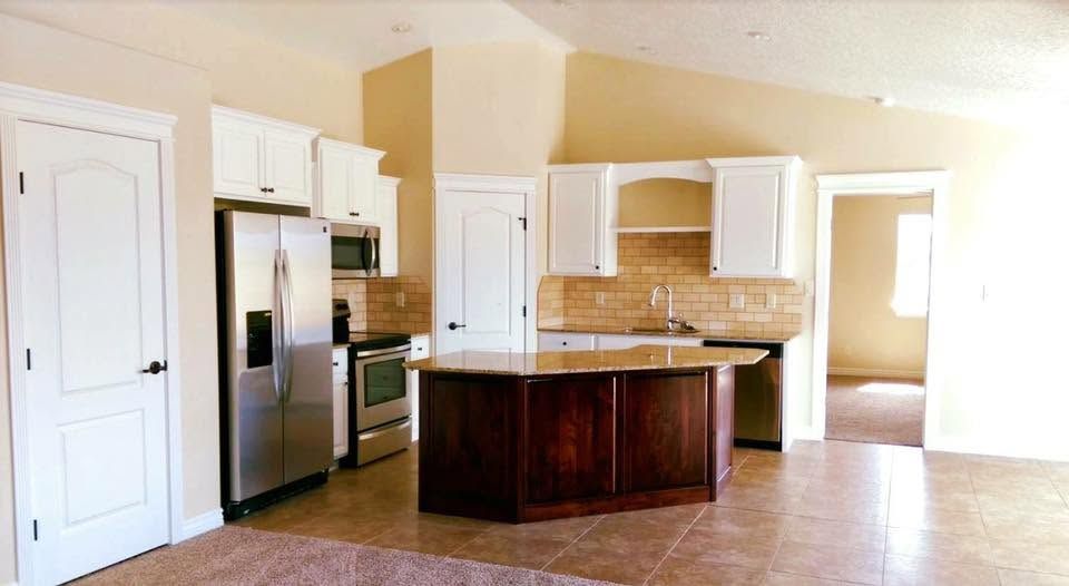 Bright modern kitchen with white cabinets, stainless fridge, and dark wood island open to a tiled dining area