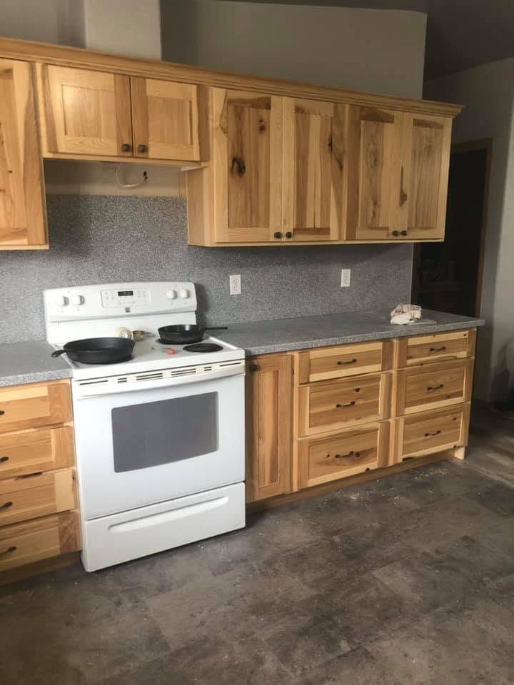 Small kitchen with light wood cabinets, white stove, gray countertops, and dark concrete floor.
