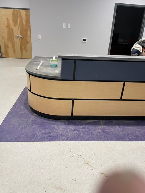 Empty reception desk with wood and dark blue panels on a purple floor mat in a lobby.